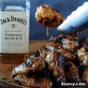 Tennessee Honey-Glazed Grilled Chicken Wings 12 holding wing with tongs with glaze dripping off near bottle of Jack Daniels Honey