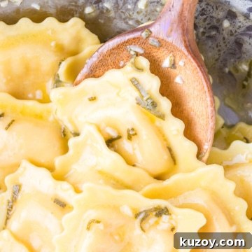 Lobster Ravioli coated in a garlic, butter, sage, and white wine sauce in a pan with a wooden spoon.