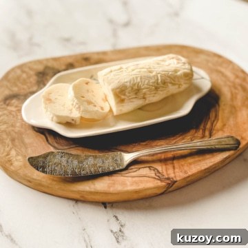 A log of roasted garlic butter is shown on a white butter dish with a butter knife.