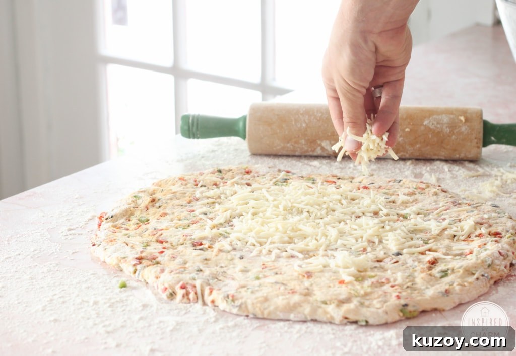 How to Make Homemade Pizza Bread (Crispy, Cheesy Recipe) 9 cheese being sprinkled onto rolled out dough
