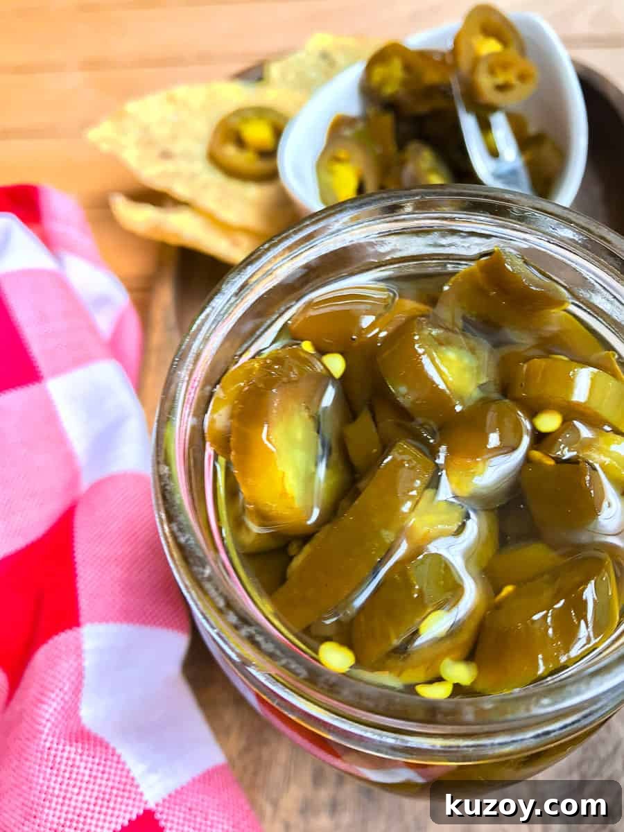 Candied jalapenos in a jar next to a red and white checkered napkin