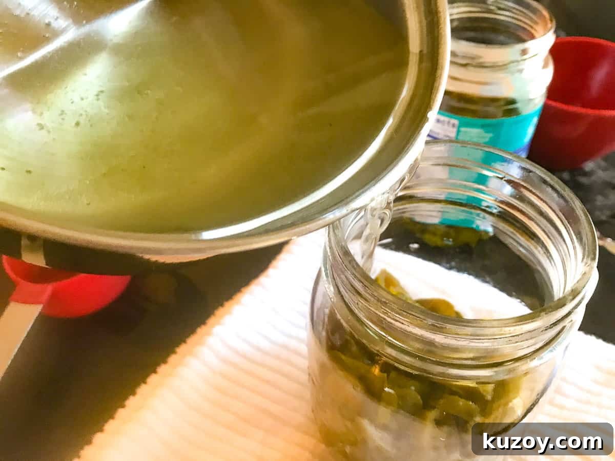 Saucepan of simple syrup being poured over jarred jalapenos