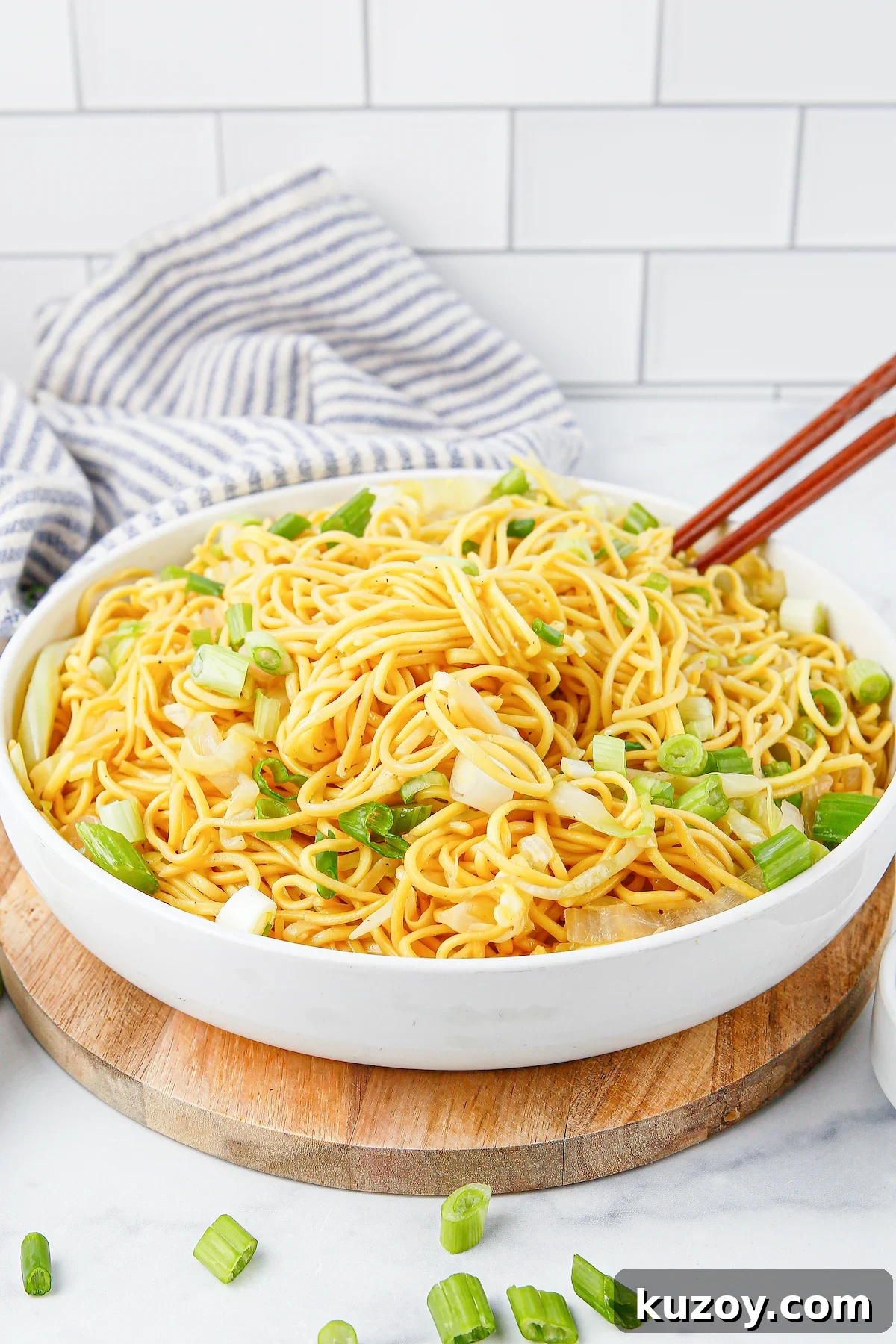 Panda Express Chow Mein Recipe: Copycat Version for Home Cooking 3 A shallow white serving bowl full of chow mein noodles that are garnished with sliced green onion and chopsticks.