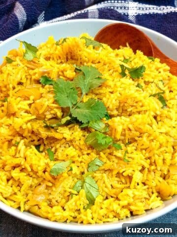 A white serving dish holding yellow pilau rice and a wooden serving spoon.