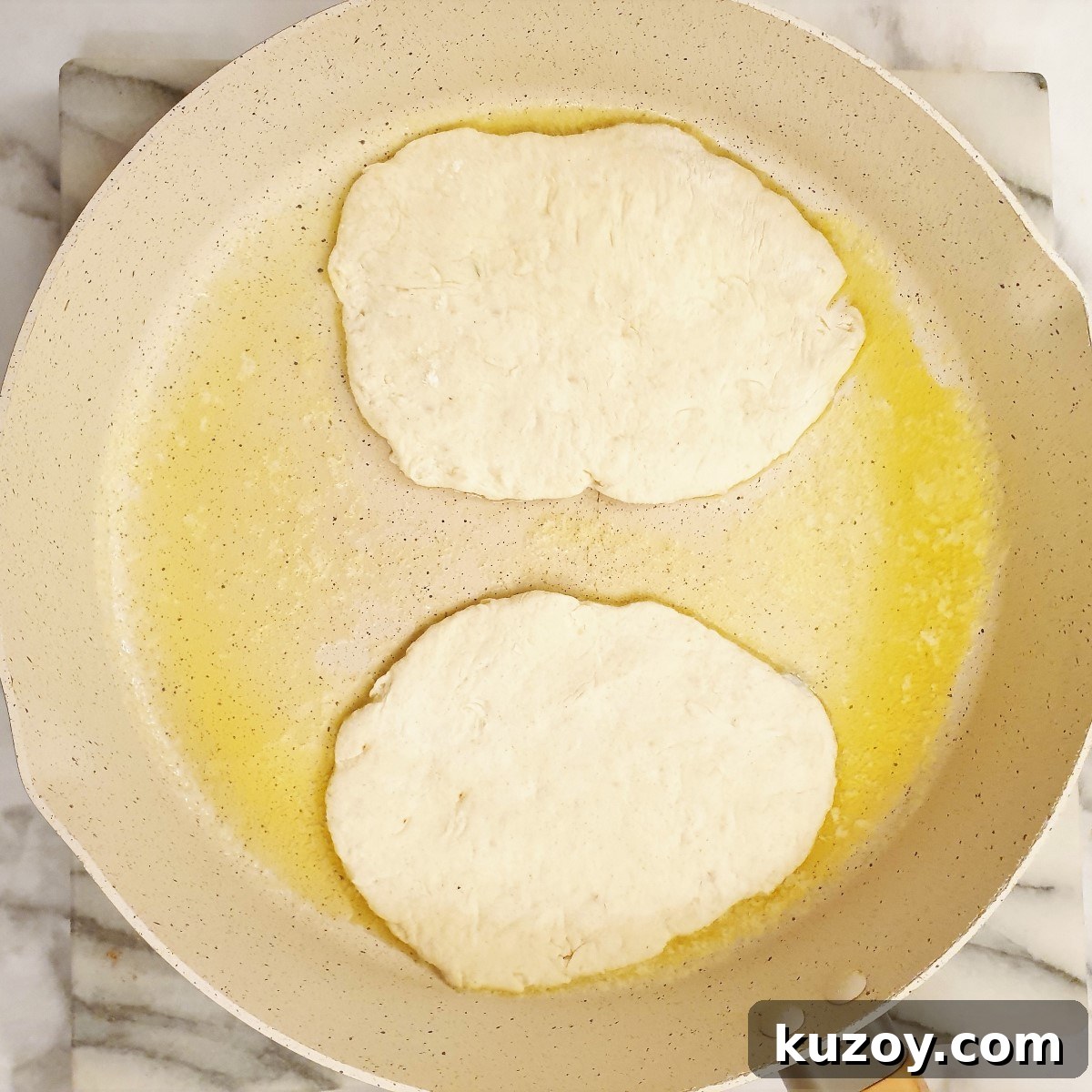 Two pieces of garlic naan bread being fried in butter.