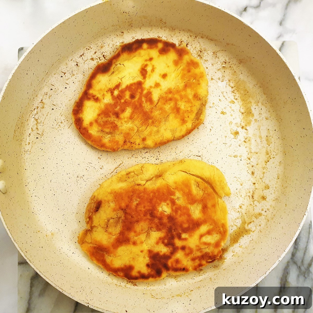 2 pieces of naan bread browning in butter in a frying pan.