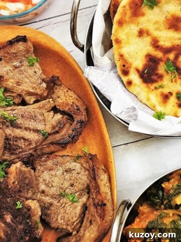 Tandori lamb chops on a plate with naan bread and saag aloo.