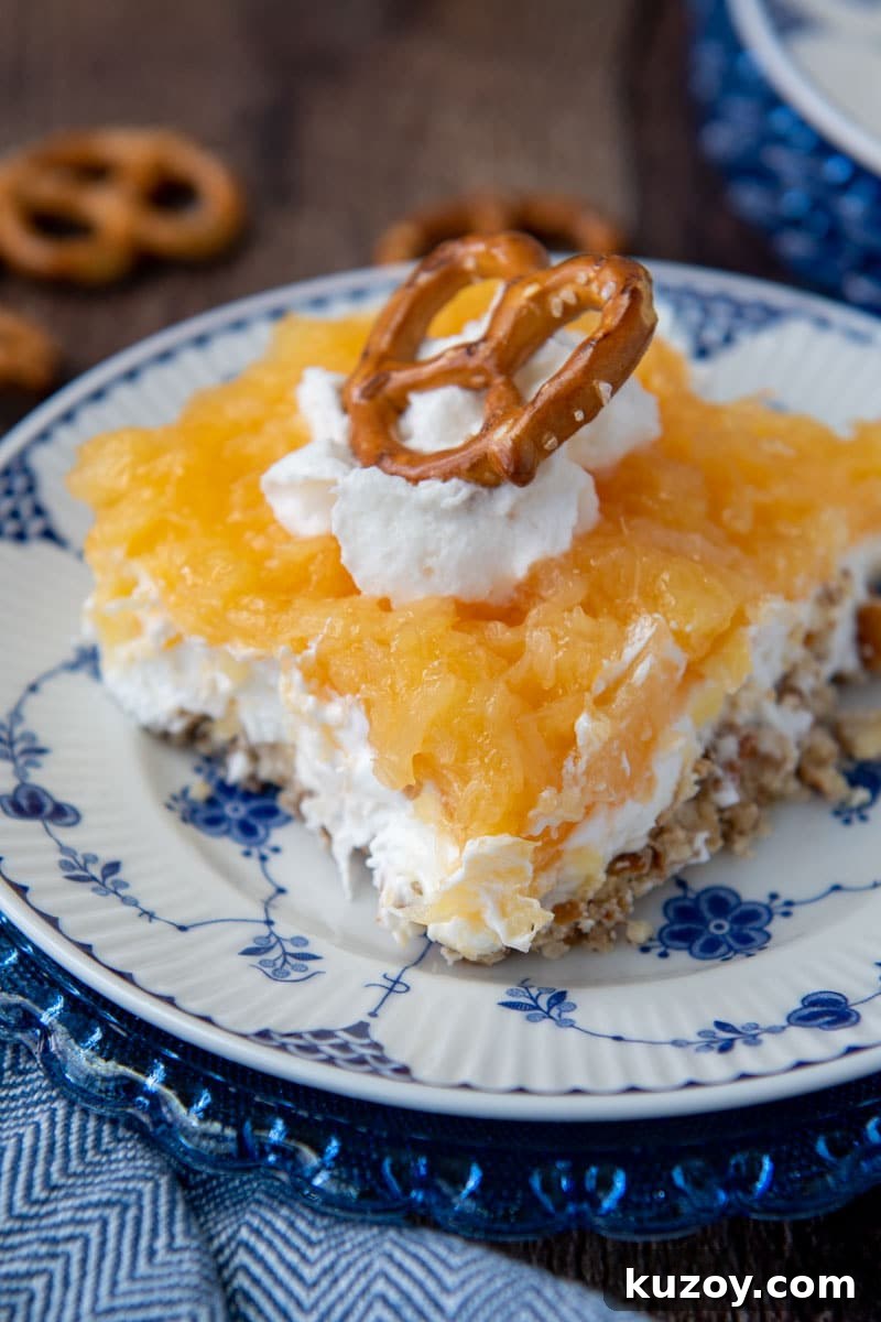 Creamy Pineapple Pretzel Salad Recipe with Crunchy Crust 2 close up of a slice of pretzel salad with pineapple with whipped cream and pretzel on top