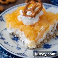 Creamy Pineapple Pretzel Salad Recipe with Crunchy Crust 6 close up of a slice of pretzel salad with pineapple with whipped cream and pretzel on top