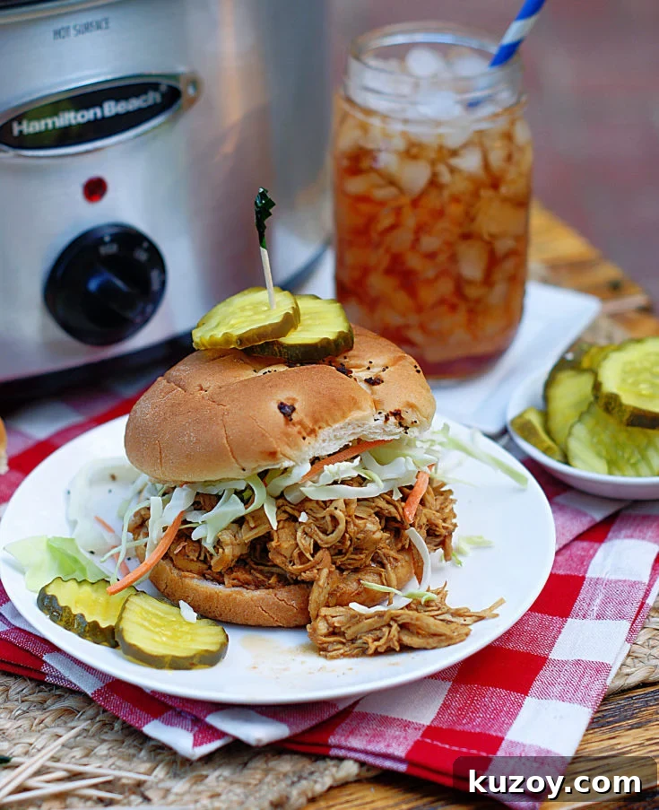 A Shredded Chicken BBQ Sandwich with pickles and a crock pot in the background.