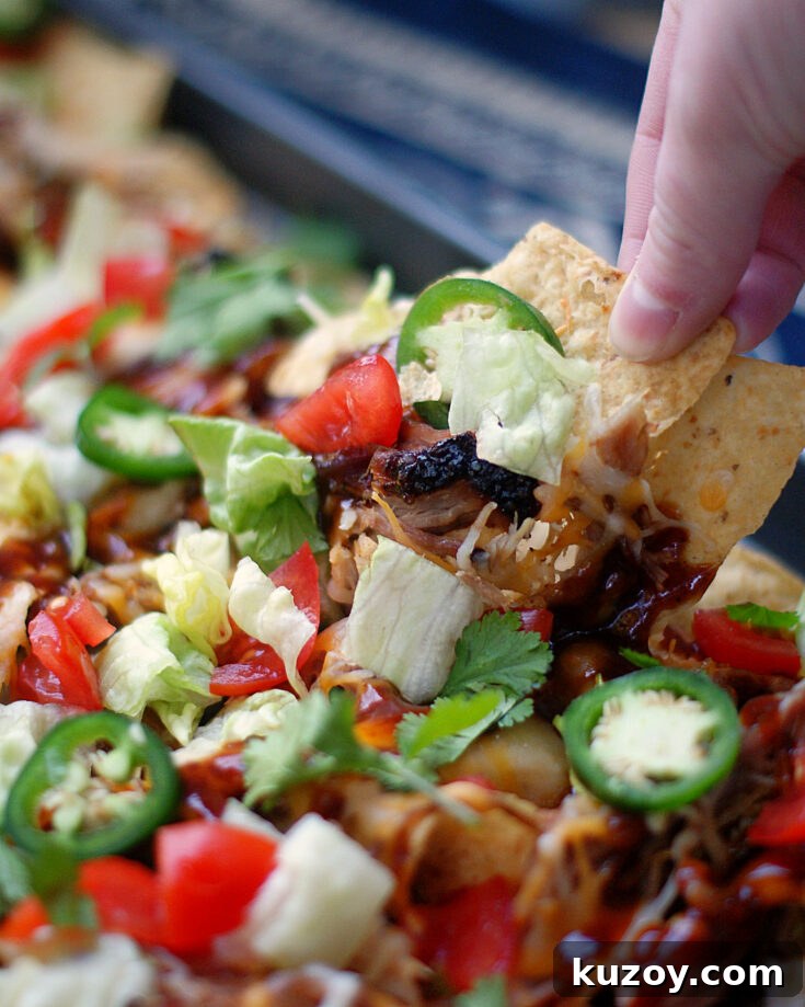 Someone pulling a nacho from a sheet pan BBQ Nacho.