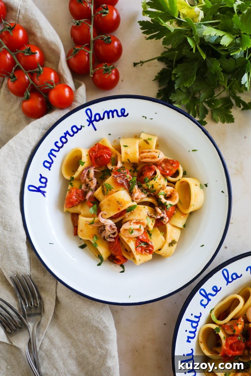 Calamarata pasta with calamari rings and tentacles and blistered tomatoes in a white and blue enamel bowl.