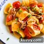 Closeup shot of Calamarata calamari and tomato pasta in a white bowl.