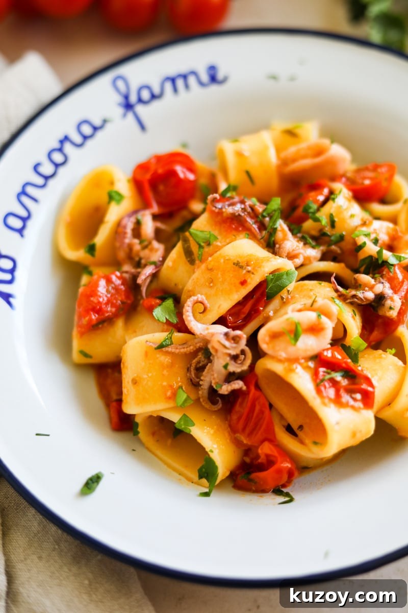 Closeup shot of Calamarata calamari and tomato pasta in a white bowl.