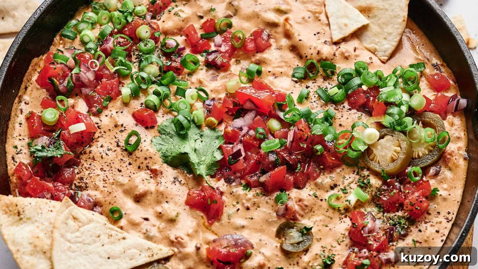 33 Must-Bring Thanksgiving Potluck Recipes for Every Year 22 A skillet filled with creamy cheese dip topped with chopped tomatoes, green onions, cilantro, and sliced jalapeños, surrounded by triangular tortilla chips.
