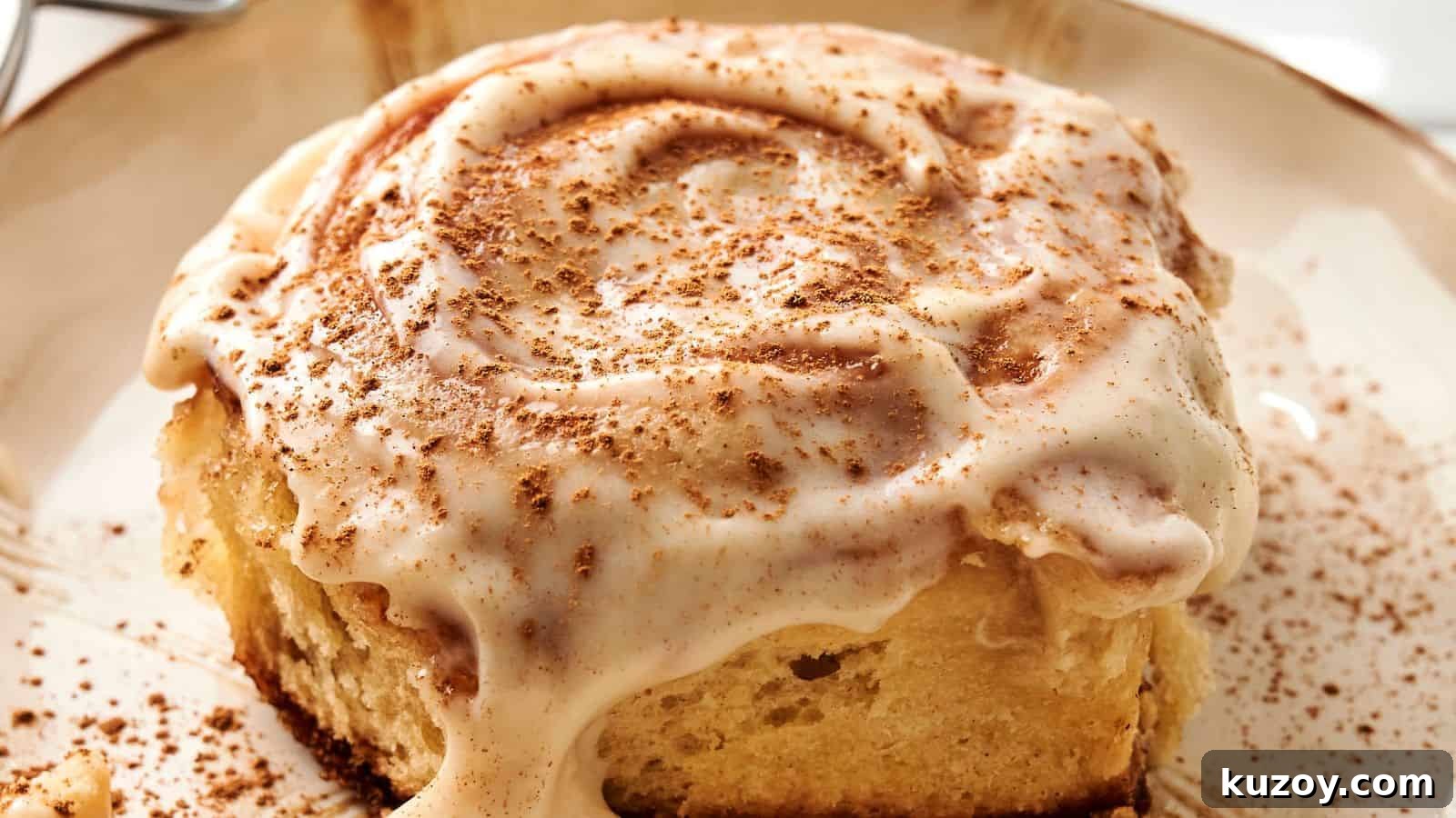 33 Must-Bring Thanksgiving Potluck Recipes for Every Year 25 A close-up of a sourdough cinnamon roll topped with creamy icing and a sprinkle of cinnamon on a plate.
