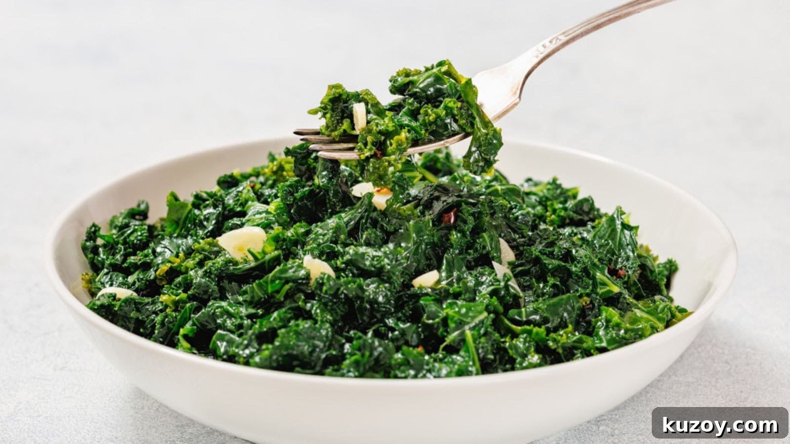 33 Must-Bring Thanksgiving Potluck Recipes for Every Year 33 A white bowl filled with sautéed kale and sliced garlic, with a fork lifting a portion from the bowl.