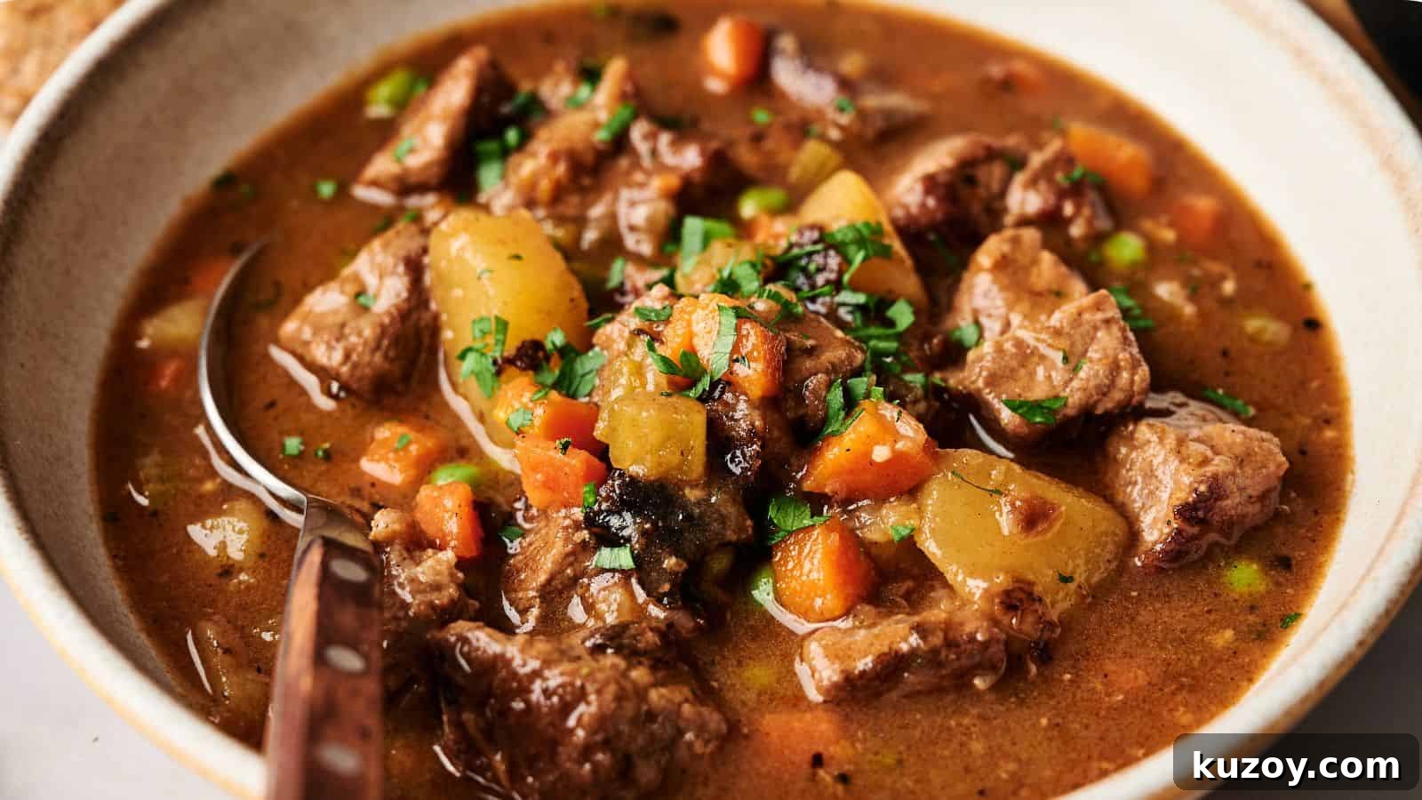 33 Must-Bring Thanksgiving Potluck Recipes for Every Year 8 A bowl of beef stew with chunks of meat, potatoes, carrots, and peas in a brown broth, garnished with chopped parsley.