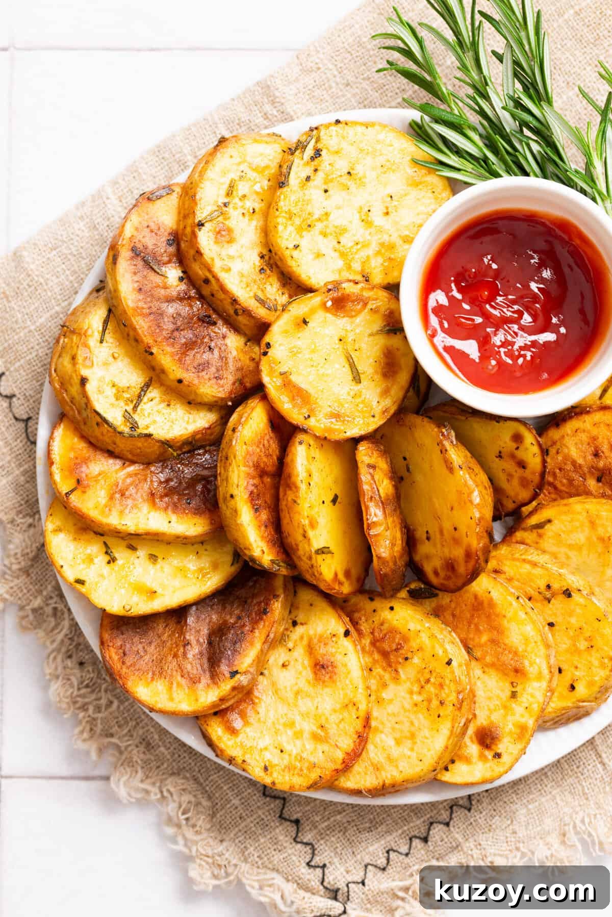 An overhead image of cottage fries arranged on a plate with a saucer of ketchup and rosemary twigs on the side.