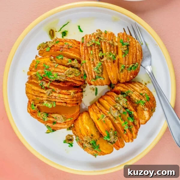 An overhead image of air fried hassel back potatoes on a plate with parsley on top and a fork and knife on the right side.