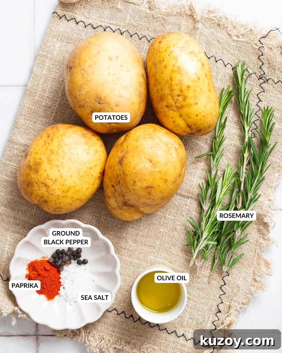 An overhead image of four russet potatoes, a spice mixture on a small plate, olive oil in a small container, and fresh rosemary twigs, with labels.