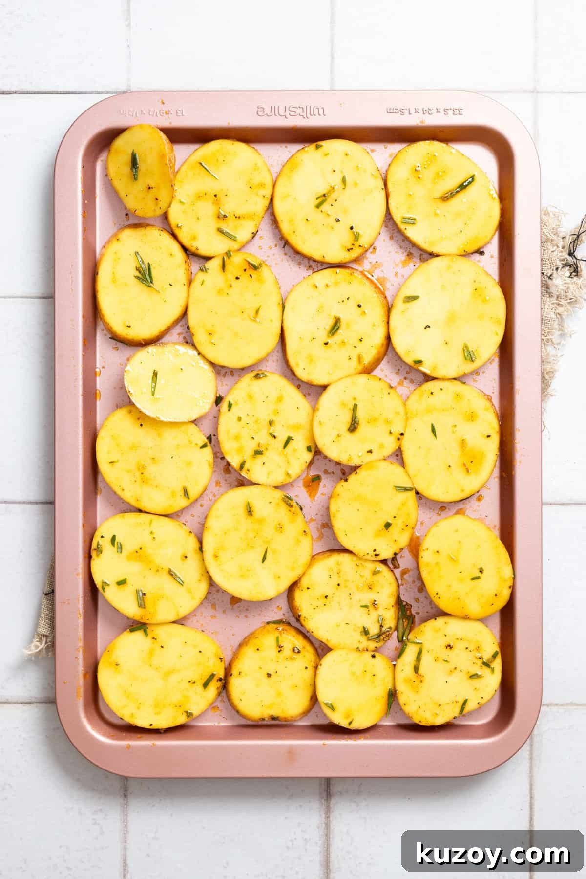 An overhead image of uncooked potatoes slices arranged side by side on a baking sheet.