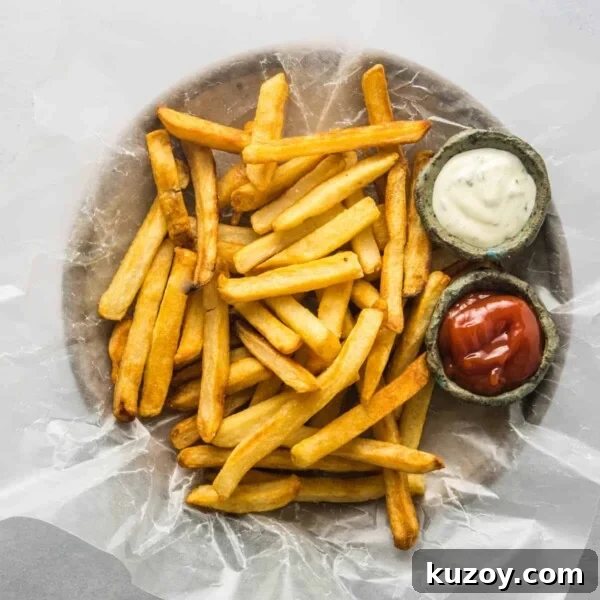 Close up of air fryer French fries on a plate with ketchup and ranch dipping sauces