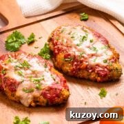 Two keto chicken parrmesan fillets on a cutting board with a tomato.