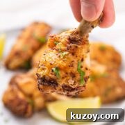 A hand holding up a crispy lemon pepper chicken drumette.