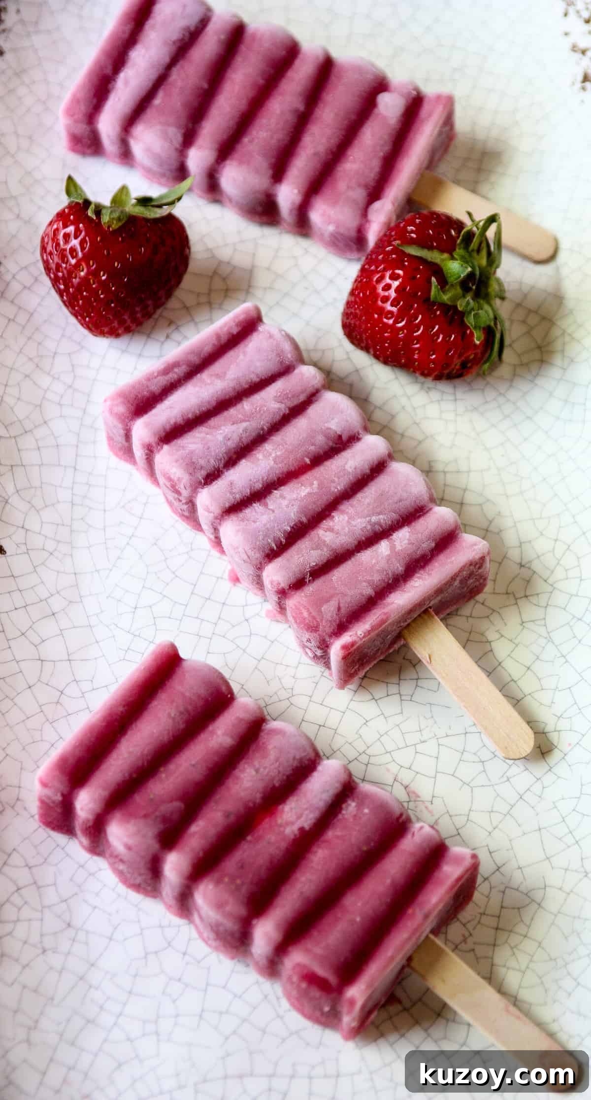 Sugar-Free Strawberry Popsicles Recipe — Fresh & Fruity 3 Two strawberry popsicles on a white speckled plate with two strawberries.