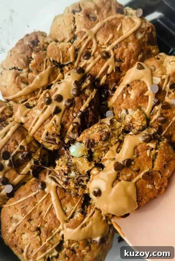 Chewy Tahini Cookies Recipe with Golden Sesame Flavor 6 A batch of oat cookies drizzled with peanut butter and sprinkled with mini chocolate chips in a glass dish, with a pink spatula lifting one cookie.