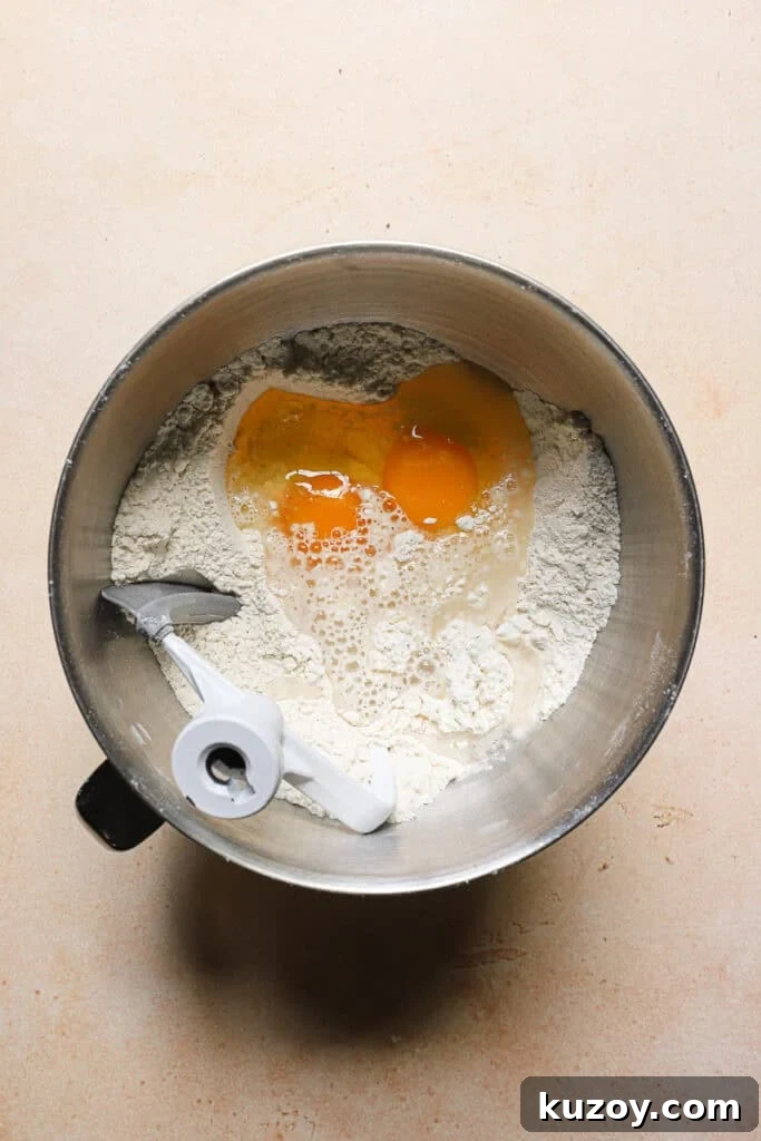 A mixer bowl with flour, eggs and the paddle attachment.
