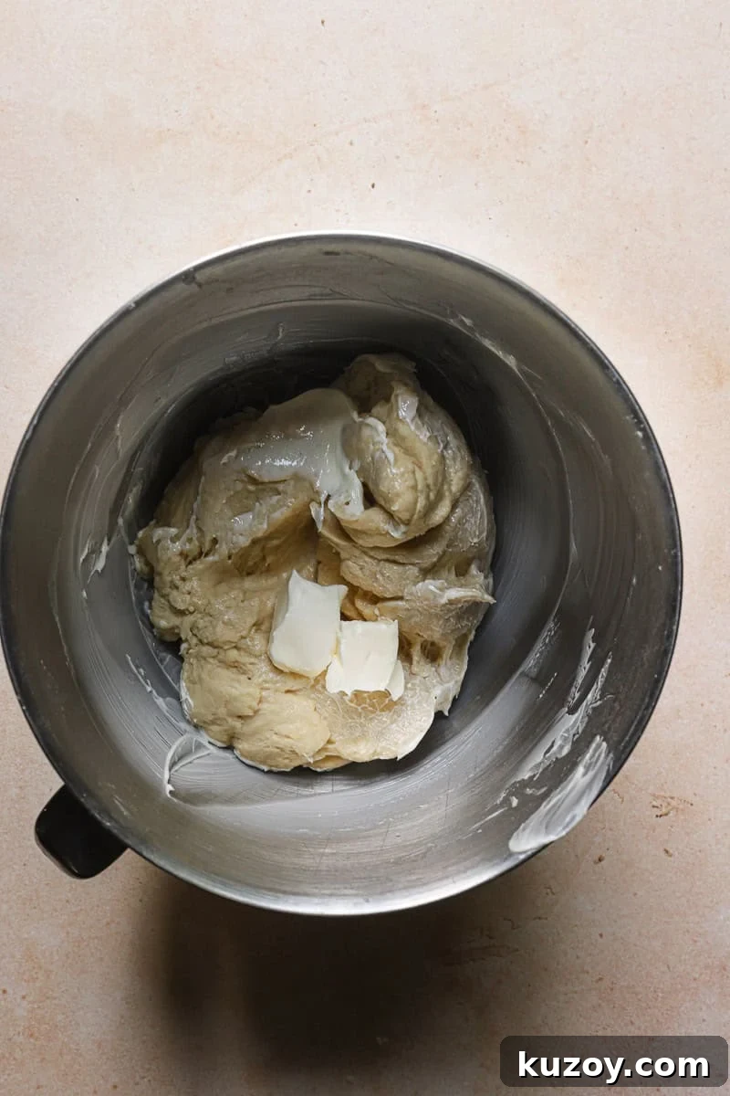 A mixer bowl with dough and two pieces of butter..