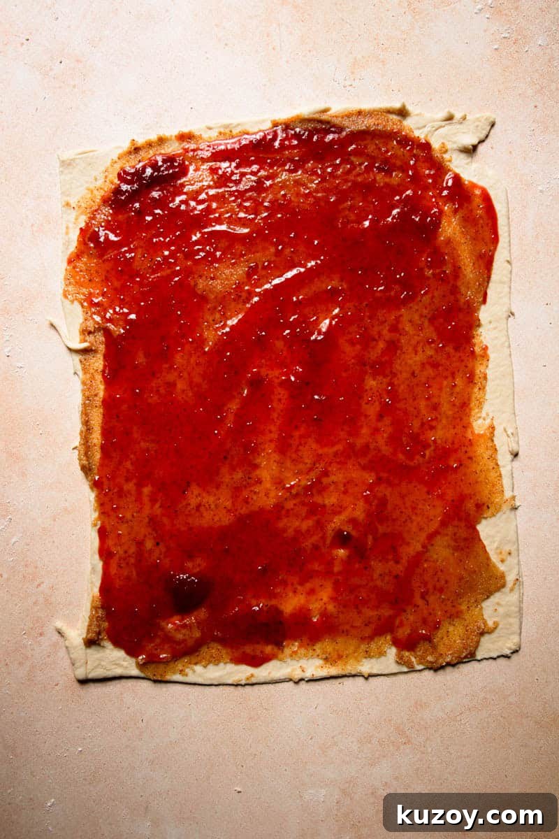 A rolled rectangle dough topped with almond cream, and a layer of strawberry preserves.