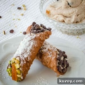How to Make Classic Cannoli Filling at Home 8 Two filled cannoli resting on each other on a white plate.