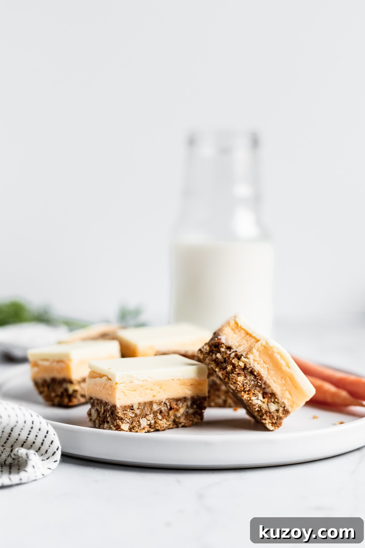 Carrot Cake Nanaimo Bars Recipe — Moist Spiced Dessert Bars 2 Sliced carrot cake bars on a white plate with a glass milk bottle in the background