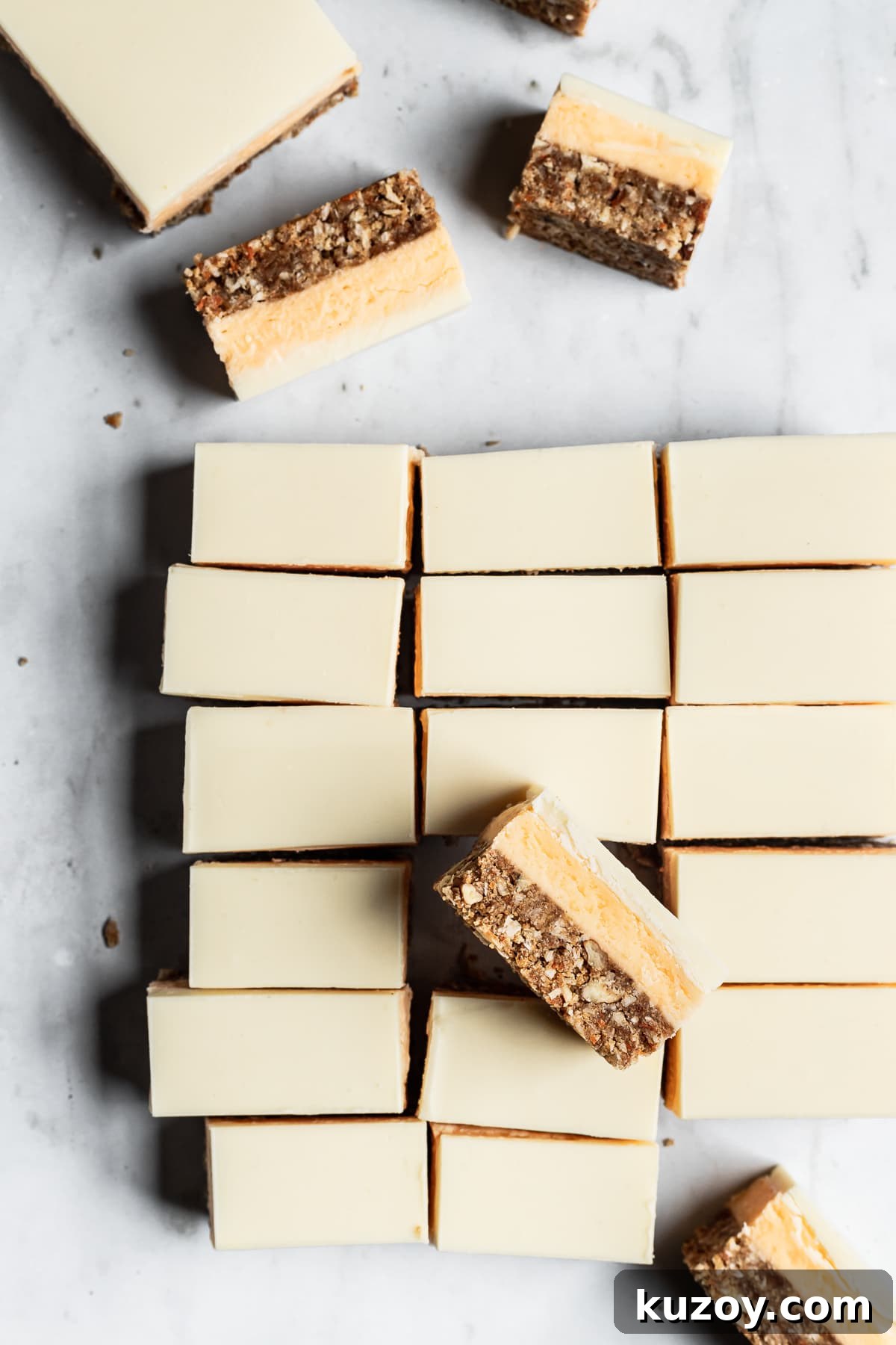 Carrot Cake Nanaimo Bars Recipe — Moist Spiced Dessert Bars 3 A grouping of bar cookies on a white marble background cut into slices with some turned on their side to show the layers