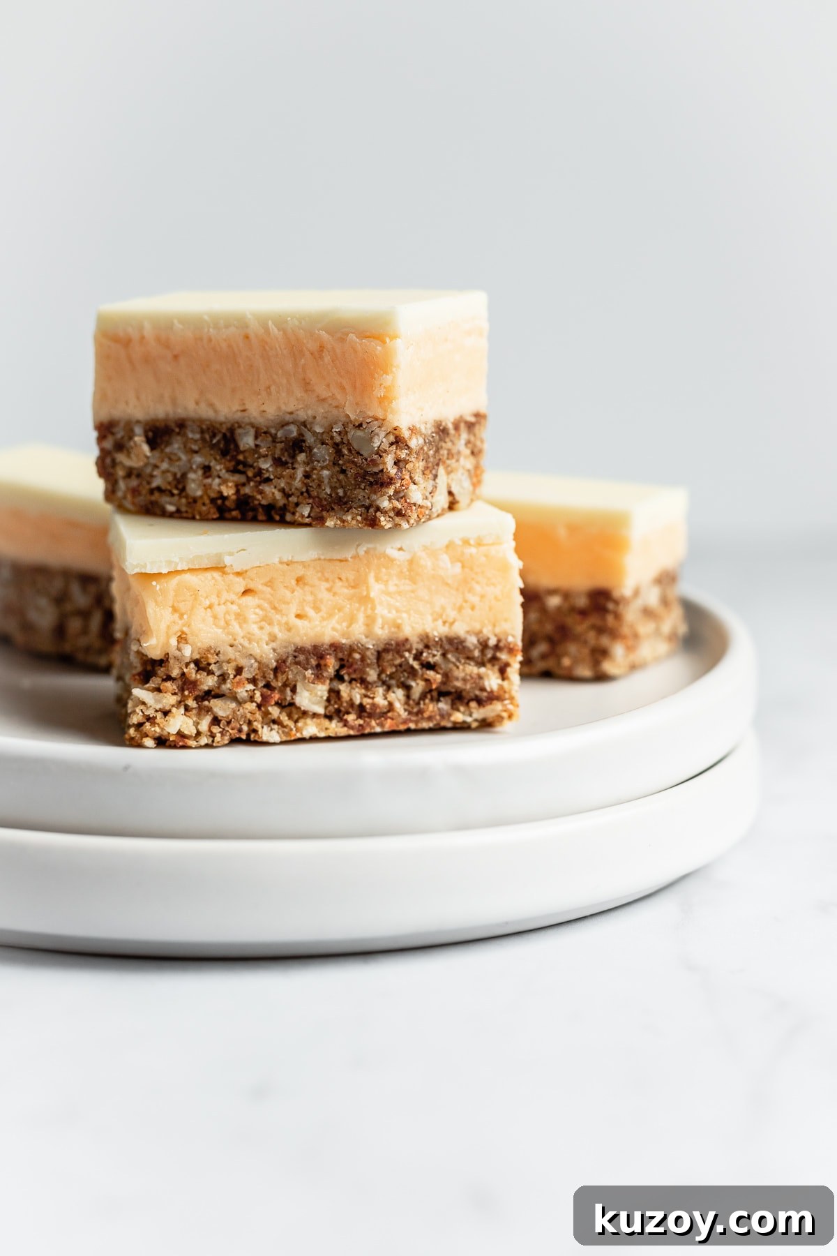 Carrot Cake Nanaimo Bars Recipe — Moist Spiced Dessert Bars 6 Sliced carrot cake bar cookies stacked up on a white plate and a white marble background