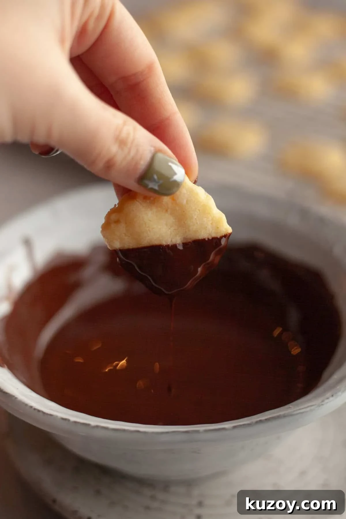 Double-Ginger Shortbread Cookies: Chewy Ginger & Crystallized Chip Recipe 9 A hand dipping a shortbread cookie in melted chocolate.