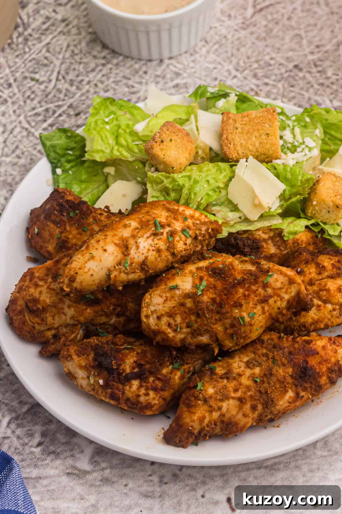 Crispy Air Fryer Blackened Chicken Tenders 7 blackened chicken tenders on a white plate with a side salad.