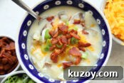 A dark blue white polka dotted soup bowl of loaded baked potato soup topped with sliced green onions, shredded cheddar cheese, and bacon crumbles.