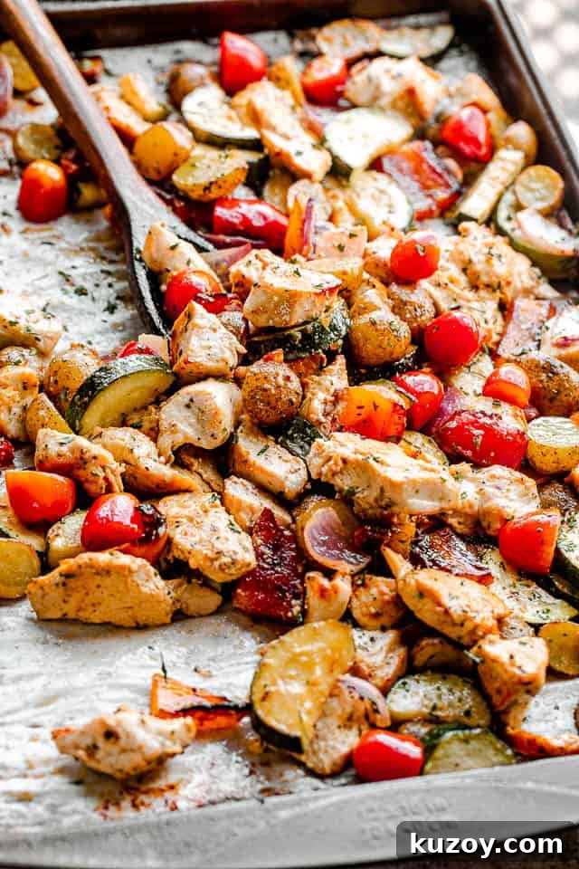 One-Pan Roasted Chicken with Seasonal Vegetables 4 side view of mixing chicken and vegetables on a baking sheet with a brown wooden spoon
