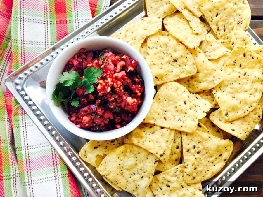 Festive Cranberry Salsa Recipe for Holiday Entertaining 2 Overhead photo of Cranberry Holiday Salsa in a white bowl with tortilla chips on a silver platter. A festive green and red towel is in the background.