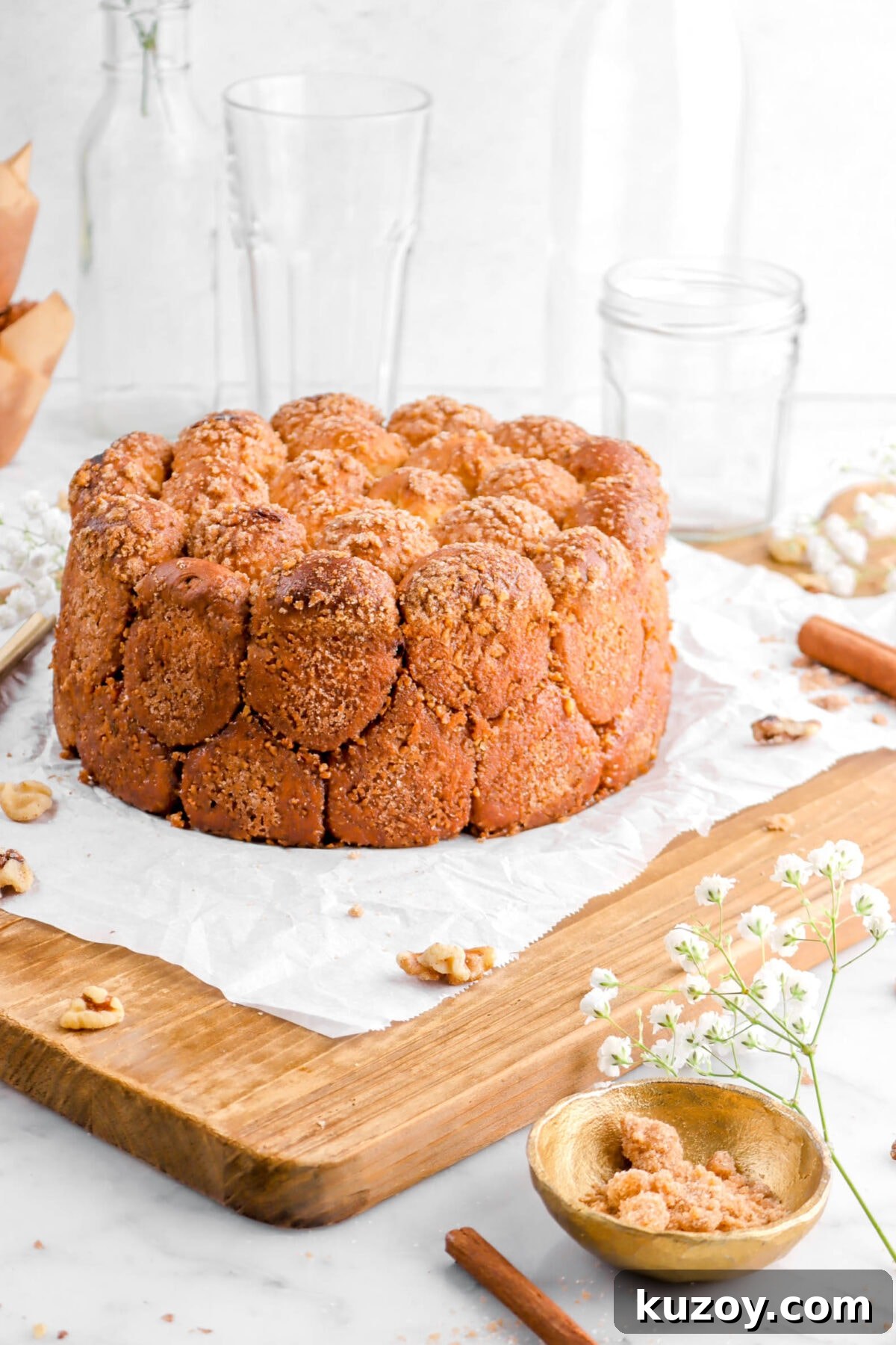 Cinnamon Sugar Walnut Pull-Apart Bread Recipe 24 angled close up of cinnamon sugar pull apart bread on wood board with walnuts, bowl of streusel, and flowers beside