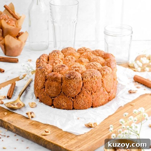 Cinnamon Sugar Walnut Pull-Apart Bread Recipe 26 cinnamon sugar walnut pull apart bread on crumbled parchment paper on a wood board with walnuts, cinnamon sticks, a gold spoon and bowl beside, a stack of muffins, an empty glass, and flowers behind
