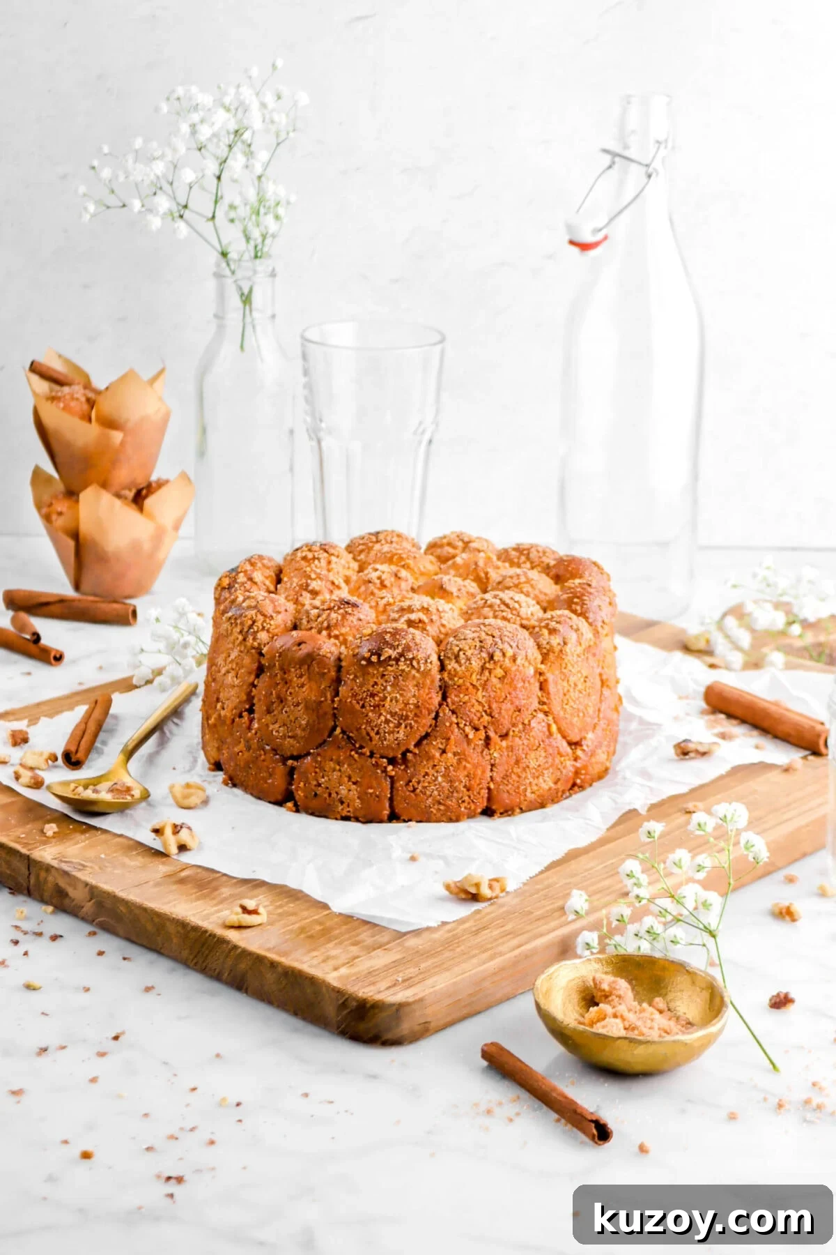 Cinnamon Sugar Walnut Pull-Apart Bread Recipe 5 bread on parchment paper on wood board with cinnamon sticks and walnuts around, with flowers, gold bowl, and gold spoon beside