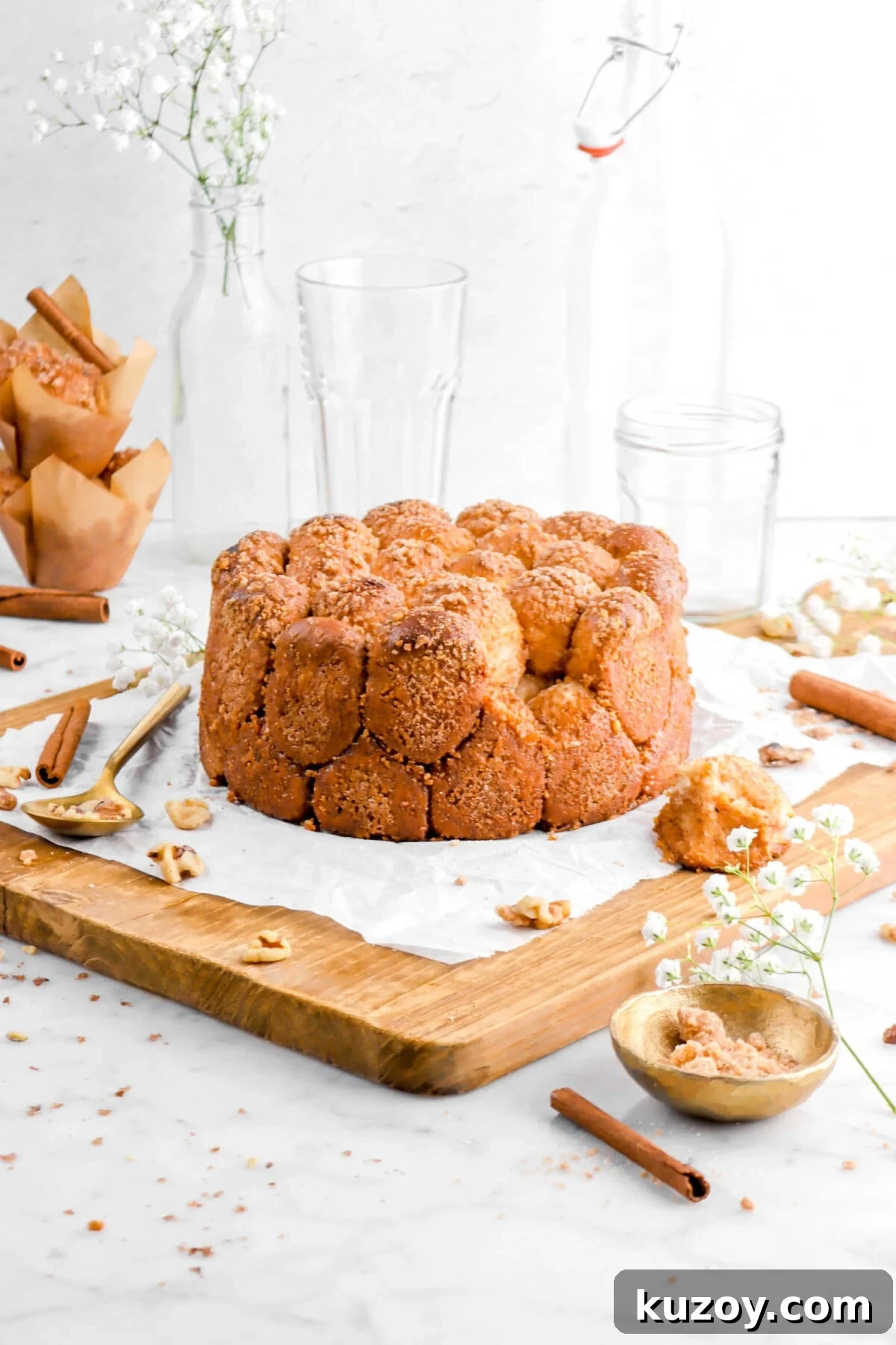 Cinnamon Sugar Walnut Pull-Apart Bread Recipe 6 pull apart bread with piece laying beside on wood board with cinnamon sticks, walnuts, and stack of muffins behind with empty glasses