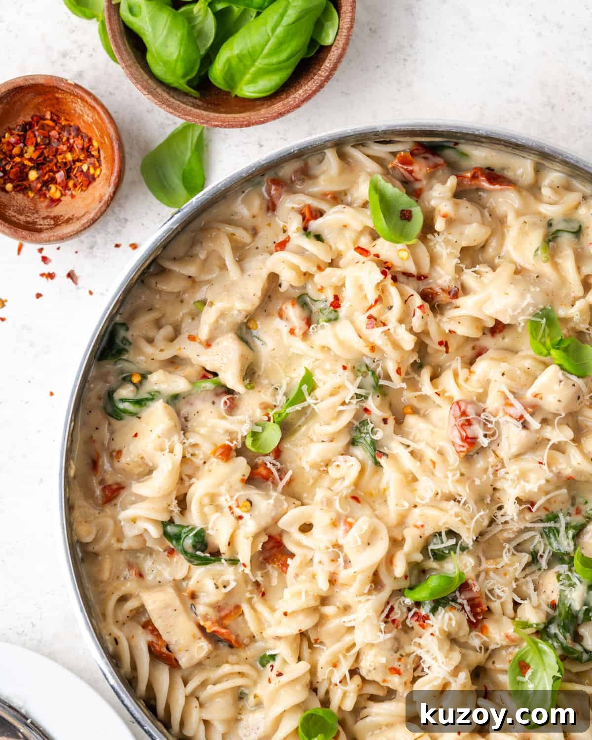 30-Minute Marry Me Chicken Pasta Recipe for Date Night 14 A pan filled with marry me chicken pasta that has been garnished with basil leaves, red pepper flakes and freshly grated cheese.