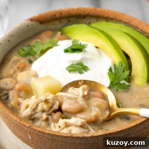 A bowl of white chicken chili topped with sour cream and sliced avocado.
