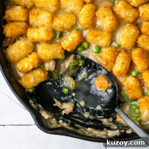 A cast iron skillet filled with chicken casserole with tater tots.